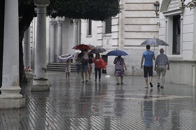 Varios melillenses, ayer en la calle refugiándose de la lluvia con sus paraguas