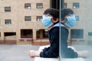 Un niño con una mascarilla se asoma a la ventana de su casa durante el confinamiento por el coronavirus