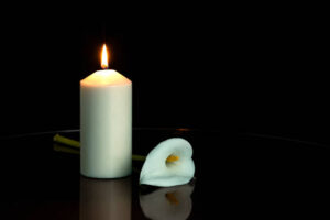 WHITE CALLA FLOWER NEXT TO A LIGHTED CANDLE ON DARK BACKGROUND. COPY SPACE.