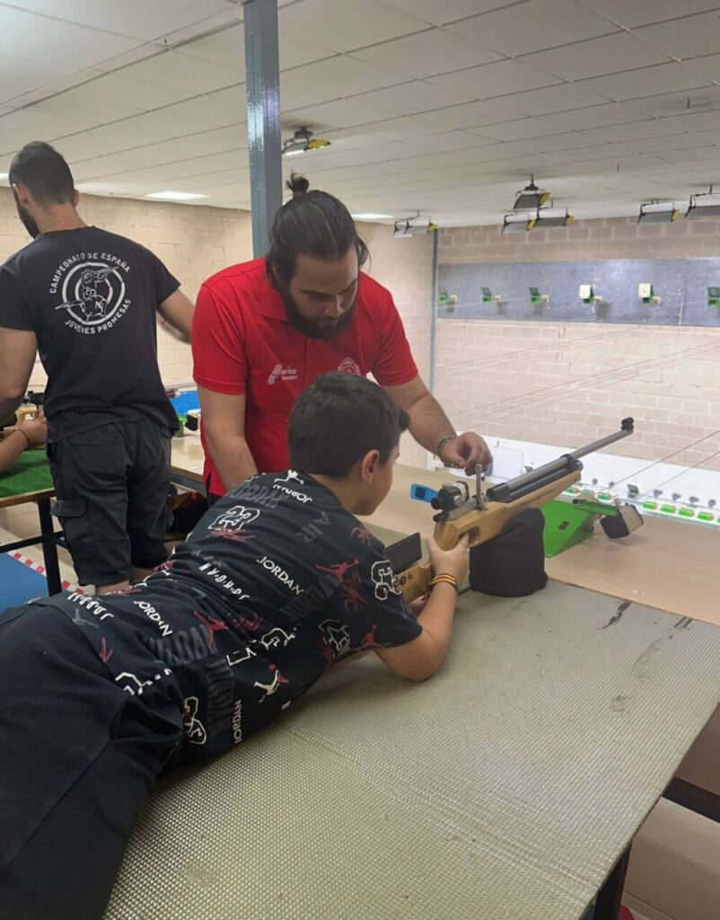 Niño practicando tiro con carabina bajo la supervisión de un monitor
