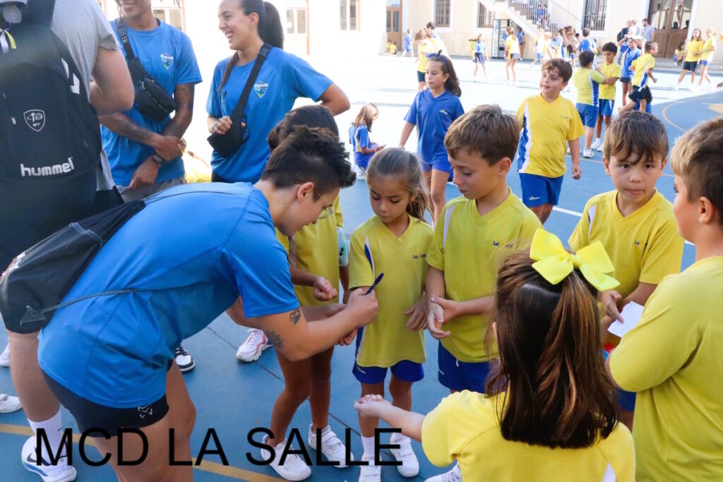 Jugadora de baloncesto firmando autógrafos a niños en el colegio.
