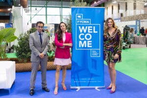 Tres personas posando junto a un cartel de FYCMA en un evento