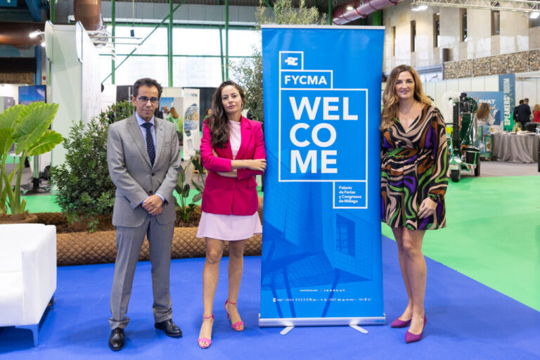 Tres personas posando junto a un cartel de FYCMA en un evento