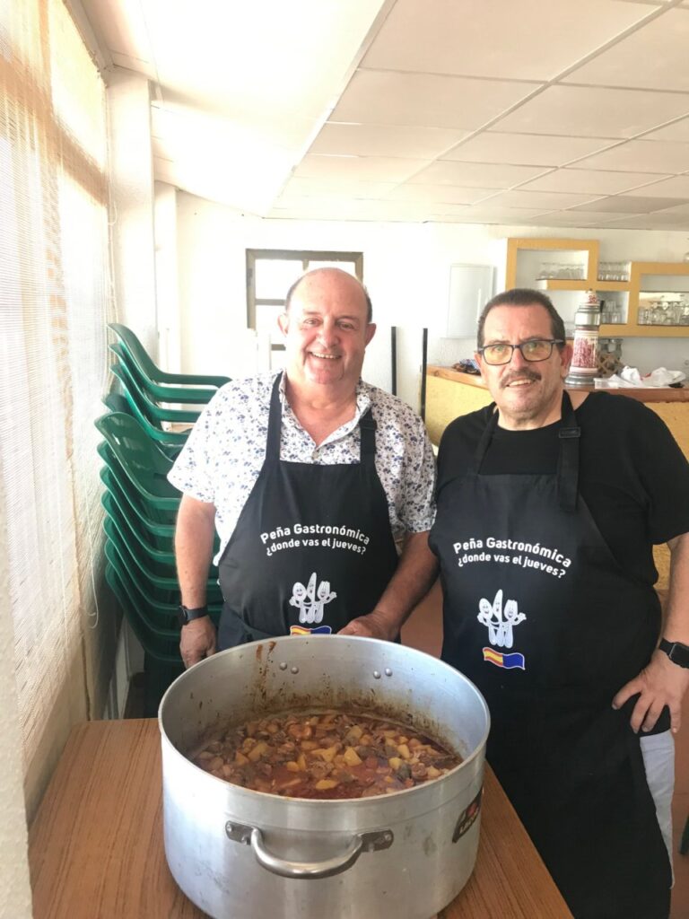 Dos chefs en la peña gastronómica con un gran plato de rancho aragonés.