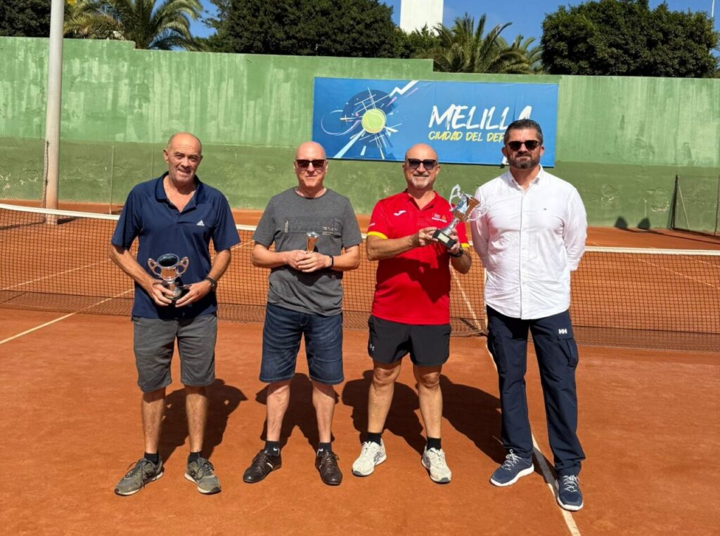 Cuatro hombres posando con trofeos en una pista de tenis en Melilla
