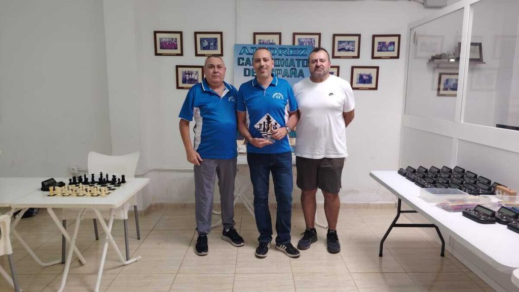 Tres hombres posando con un trofeo en un torneo de ajedrez