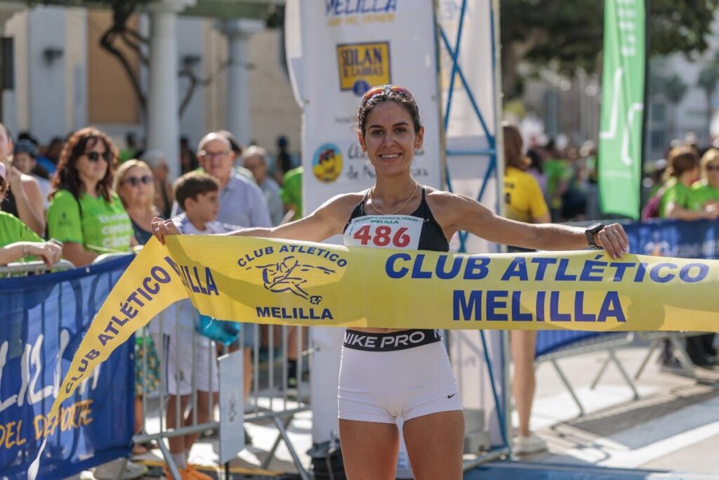 Atleta sosteniendo la cinta de meta en la carrera contra el cáncer en Melilla.