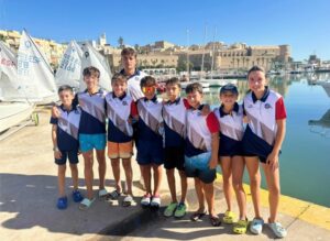 Grupo de jóvenes navegantes en el Club Marítimo con barcos de vela.