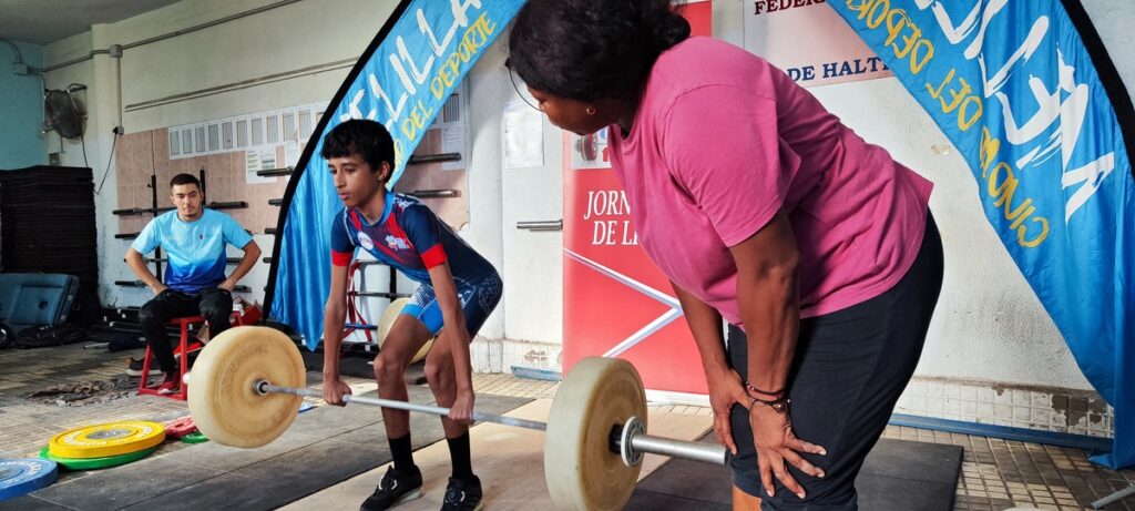 Niño levantando pesas con la supervisión de un entrenador en un evento deportivo