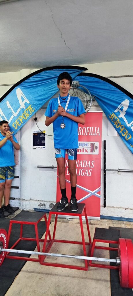 Joven levantador en el podio con medalla en competición de halterofilia.