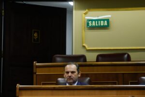 Imagen de un hombre sentado en un recinto legislativo con un letrero de salida