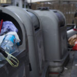 Persona depositando residuos en un contenedor de basura en la calle.