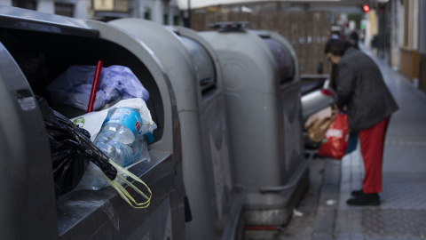Persona depositando residuos en un contenedor de basura en la calle.