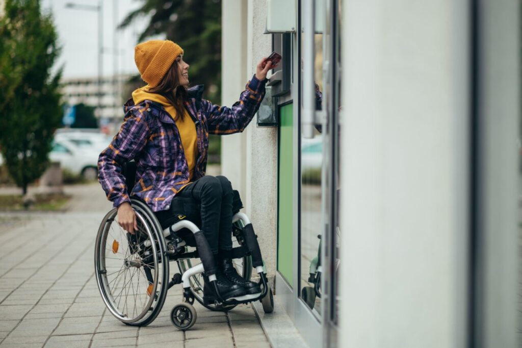 Mujer en silla de ruedas usando un cajero automático accesible.