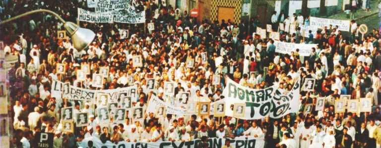 Multitud de personas en una manifestación sosteniendo pancartas y retratos.