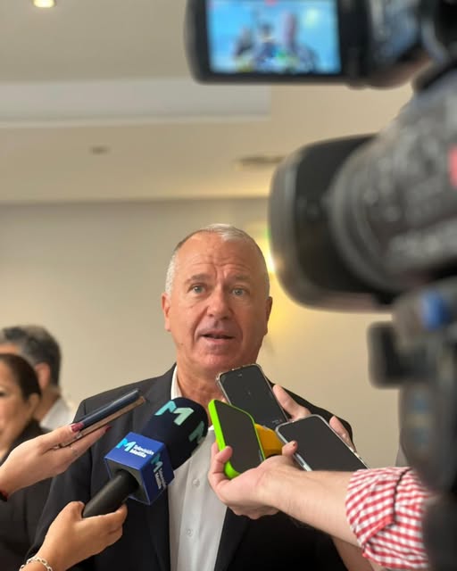 Hombre hablando a la prensa con micrófonos y cámaras alrededor.