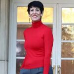 Mujer sonriente con suéter rojo frente a una puerta de cristal