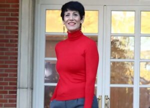 Mujer sonriente con suéter rojo frente a una puerta de cristal