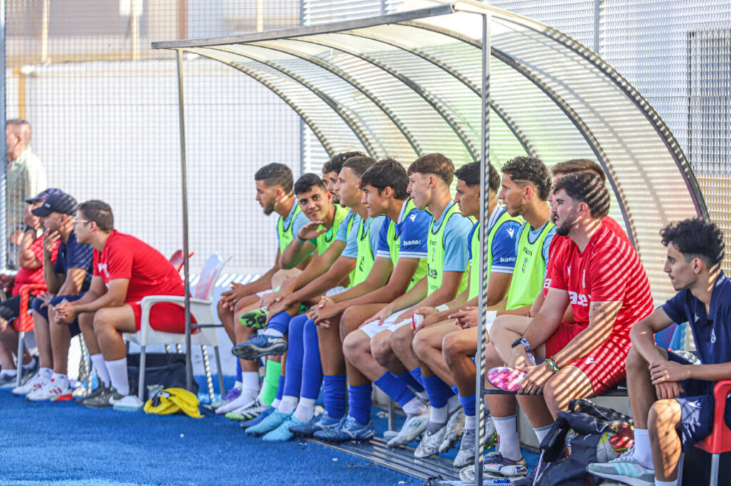 Jugadores de la U.D. Melilla B sentados en el banquillo durante un partido.