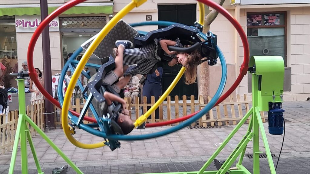 Niños disfrutando de un juego de giroscopio en la verbena popular.