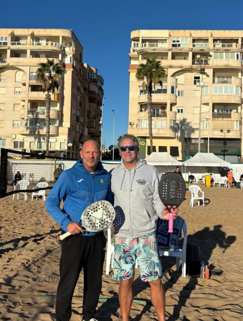 Dos hombres sosteniendo palas de tenis playa en la playa de San Lorenzo.