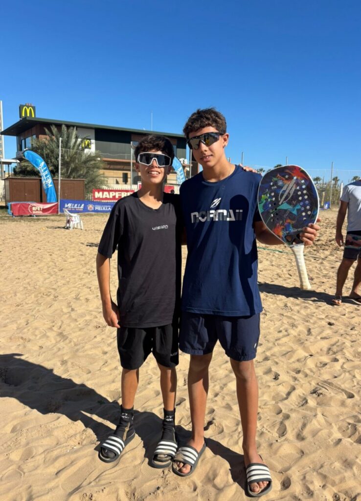 Dos jóvenes jugadores de tenis playa posando en la arena