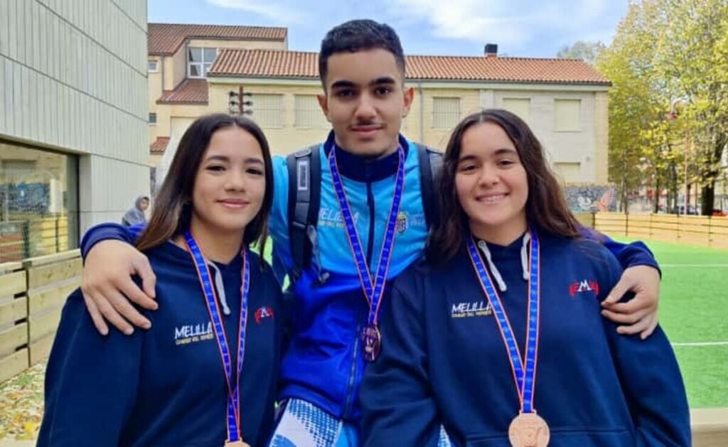 Tres jóvenes atletas melillenses posando con medallas en un evento deportivo