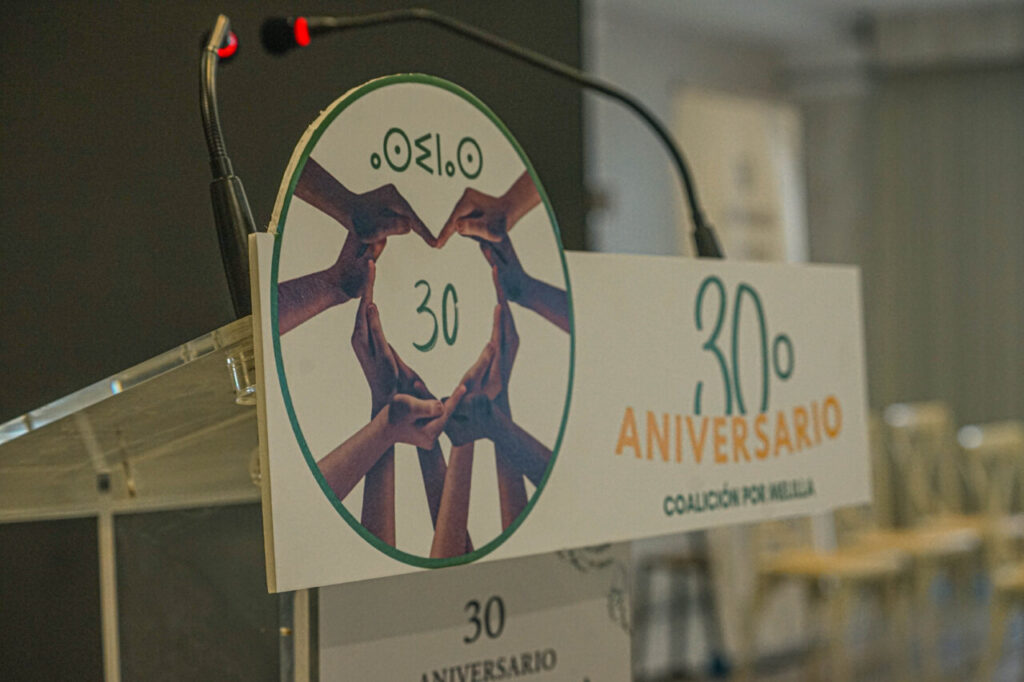 Cartel del 30º aniversario de Coalición por Melilla con manos formando un corazón.