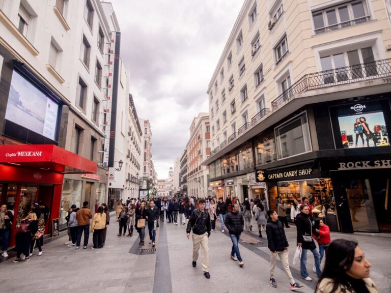 Avenida concurrida en Madrid con tiendas y gente caminando.