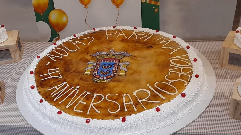 Tarta de cumpleaños con el logo de Aulas para Mayores y decoración festiva