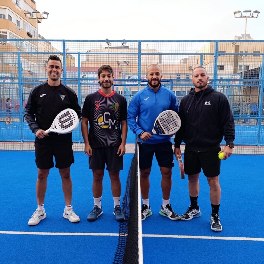Cuatro jugadores de pádel posando en una cancha azul