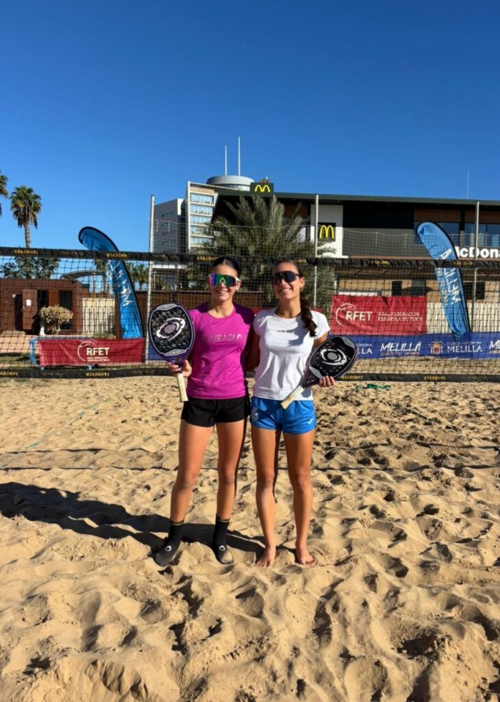 María Martínez y otra jugadora sosteniendo trofeos en la playa