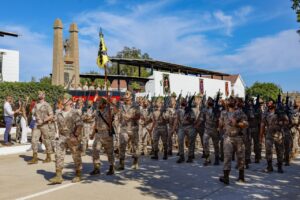 Militares marchando en una ceremonia con banderas y armas.