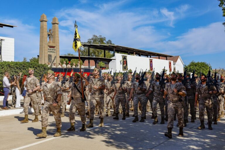 Militares marchando en una ceremonia con banderas y armas.
