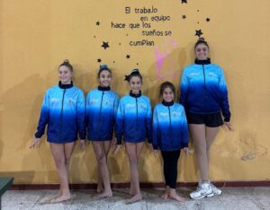 Grupo de gimnastas posando con chaquetas azules en un fondo amarillo
