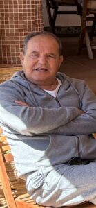 Hombre mayor sentado con sudadera gris y sonrisa cálida.