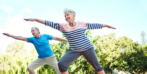 Pareja de mayores realizando ejercicios al aire libre en un entorno natural.