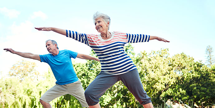 Pareja de mayores realizando ejercicios al aire libre en un entorno natural.