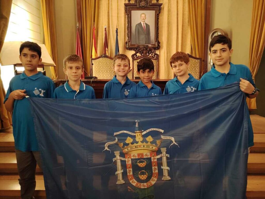 Grupo de jóvenes ajedrecistas con bandera en el salón de plenos