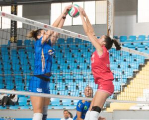 Jugadoras de voleibol en un partido disputando el balón en la red.