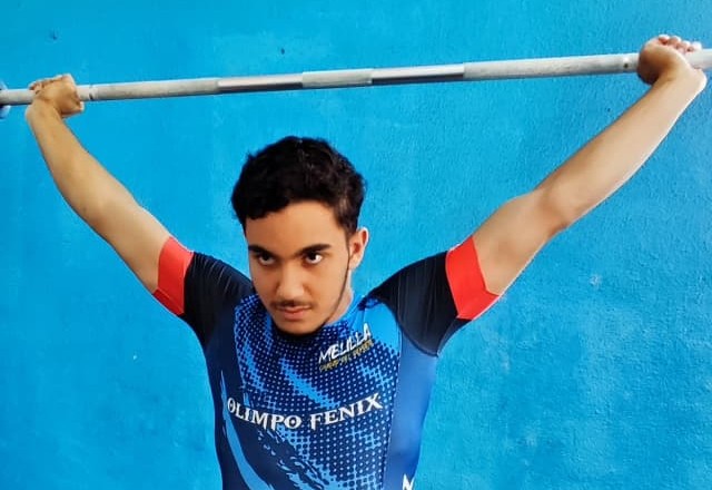 Joven levantador de pesas entrenando con barra en el gimnasio