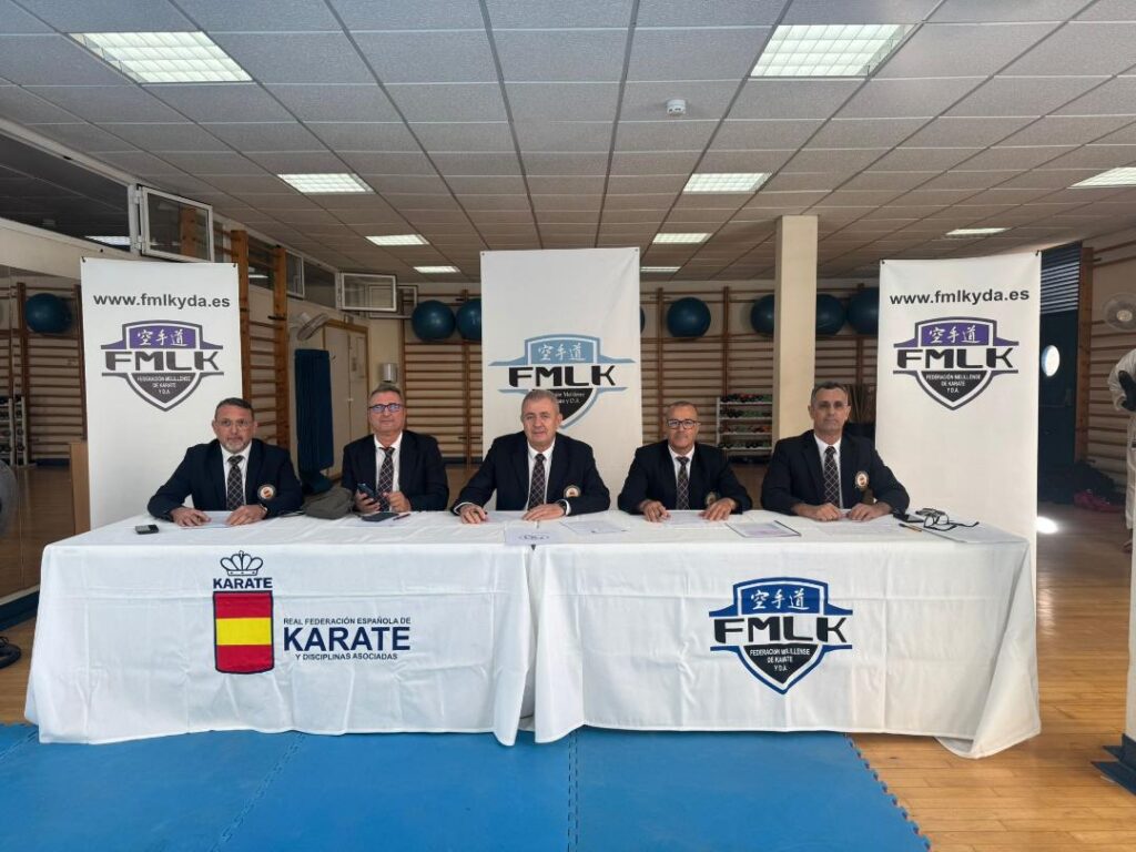 Cinco miembros del tribunal de karate en una mesa con logotipos.