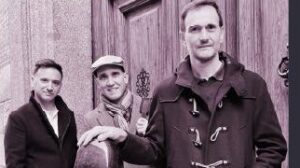 Tres músicos posando juntos frente a una puerta de madera