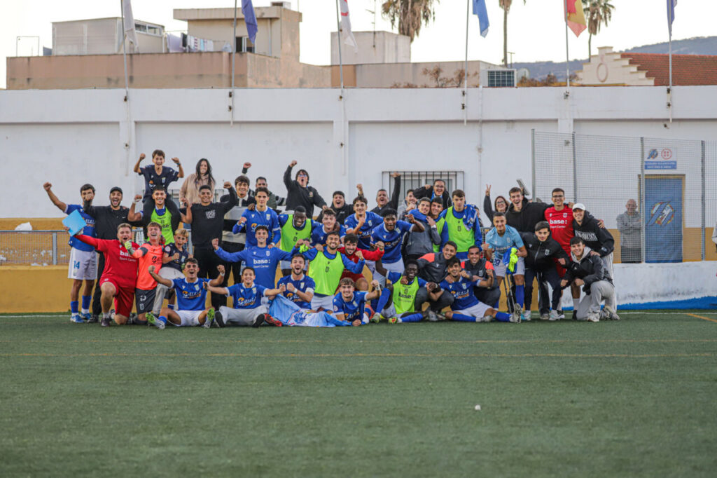 Jugadores y aficionados de la U.D. Melilla B celebrando una victoria en el campo.