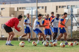 Jugadores de la U.D. Melilla entrenando en el campo con balones de fútbol.