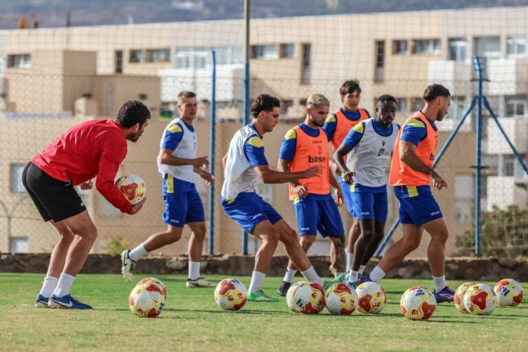 Jugadores de la U.D. Melilla entrenando en el campo con balones de fútbol.