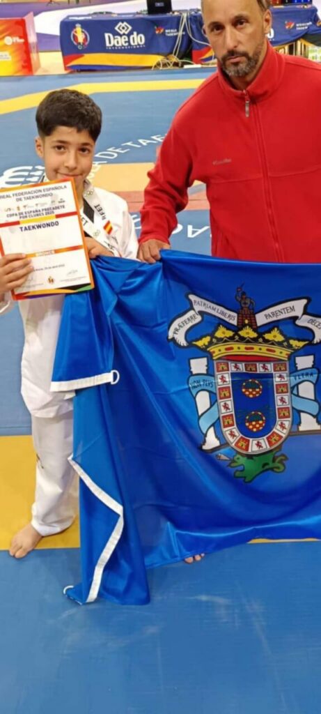 Adam sosteniendo su certificado y bandera tras ser subcampeón de taekwondo