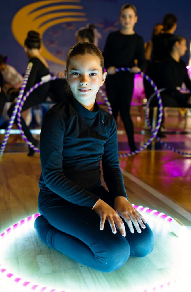 Niña sentada en el suelo con aro luminoso en el festival de gimnasia rítmica