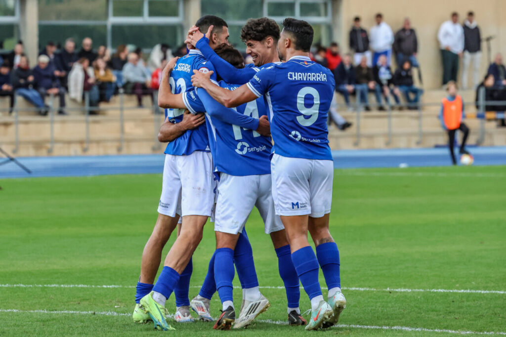 Jugadores de la U.D. Melilla celebrando un gol en el campo.