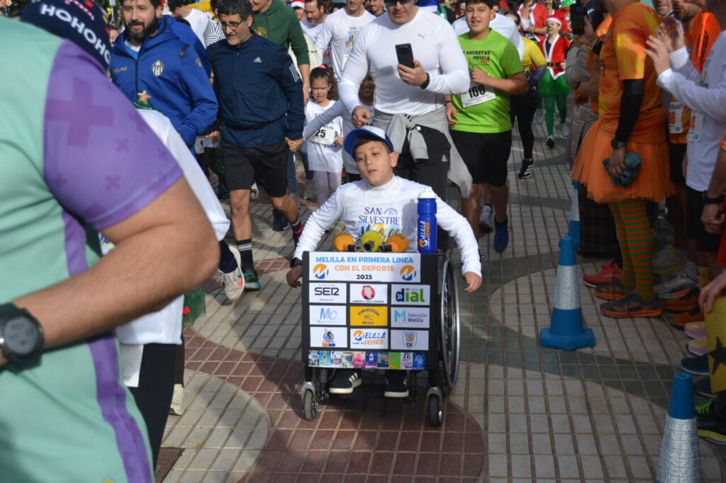 Participantes en la carrera San Silvestre de Melilla 2025 con un niño en silla de ruedas